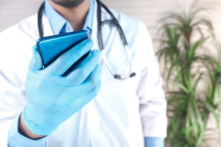 doctors hand in protective gloves using a smartphone.の写真素材