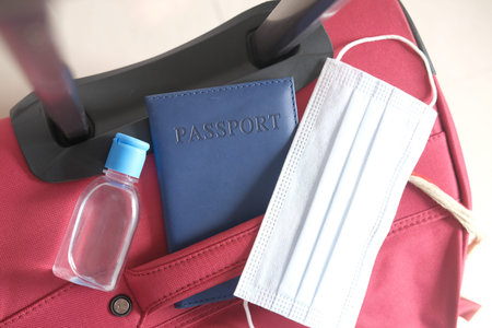 passport, hand sanitizer and face mask on suitcase on ground