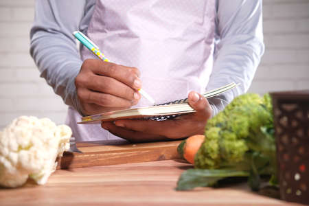 young man writing diet pan on notepad on kitchen tableの写真素材
