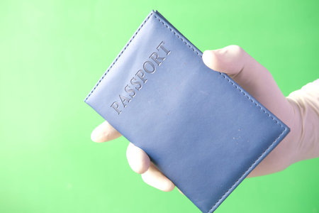 hand in blue surgical gloves holding passport in hand.