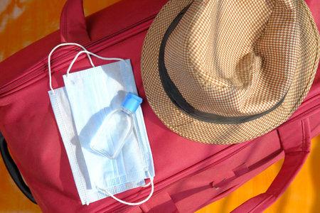 passport, hand sanitizer and face mask on suitcase on ground