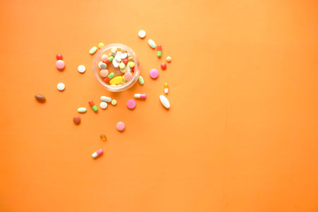 many colorful pills and capsules spilling on orange background