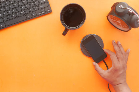 charging Smartphone using Wireless Charging Pad on orange background
