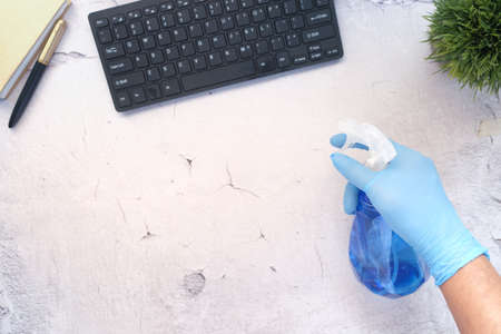 hand in blue rubber gloves holding spray bottle cleaning tableの写真素材