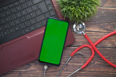 Medical Stethoscope and smart phone on laptop on wooden table