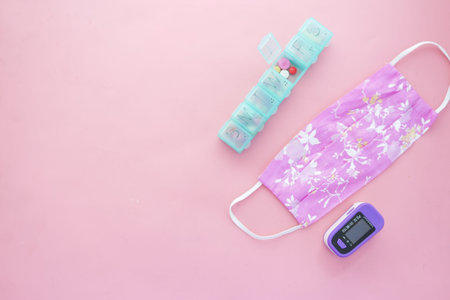 pulse oximeter, cloth mask and medical pills on pink