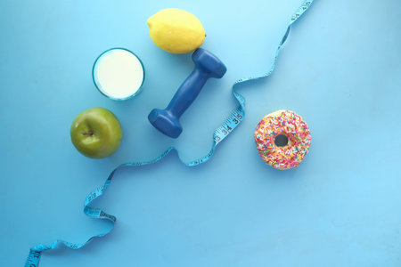measuring tape wrapped around a dumbbell and donuts on tableの写真素材