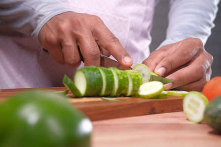 young man cutting cucumber on chopping board .の写真素材