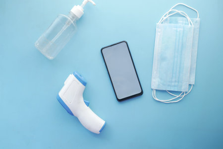 flat composition of smart phone, mask, thermometer and sanitizer on table
