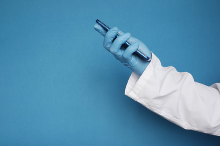 doctors hand in protective gloves using a smartphone against blue background