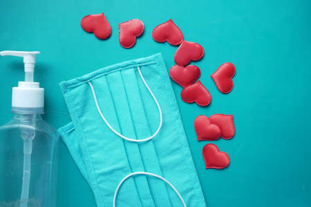 Surgical masks with heart shape and hand sanitizer on color backgroundの写真素材