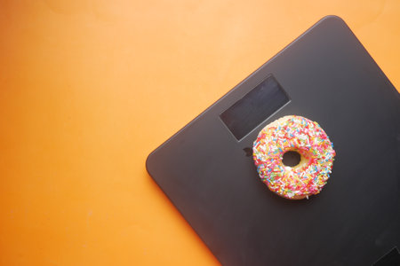 sweet donuts on weight scale on orange backgroundの写真素材