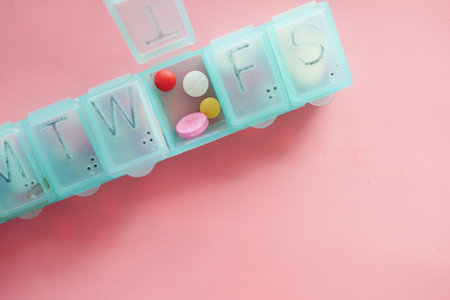 medical pills and capsule in a pill box on pink backgroundの写真素材