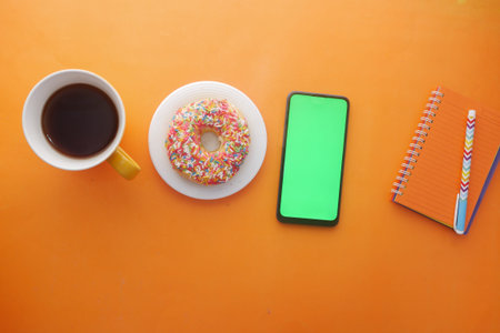 top view of coffee , donuts , notepad and smart phone on orange background