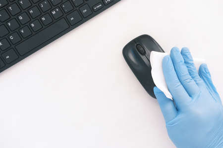 hand in blue rubber gloves and white tissue disinfecting computer mouseの写真素材
