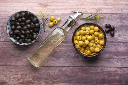 bottle of olive oil, fresh green and black olive in a container on table .の写真素材