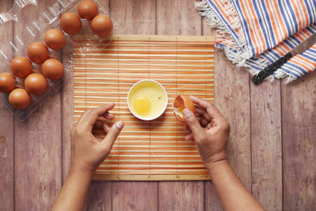 man breaking egg and pouring into a small container on table ,の写真素材