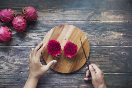 young man cutting a dragon fruit on a chopping board.の写真素材