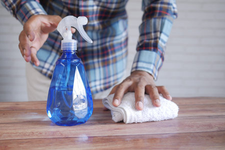 hand in blue rubber gloves holding spray bottle cleaning table