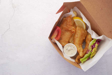 Fish fillet, lemon , chips and potato mash in take away box on tableの写真素材