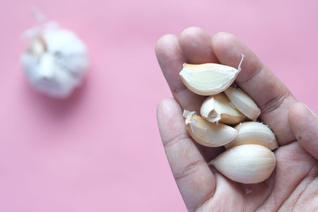 close up pf garlic on hand against pink background
