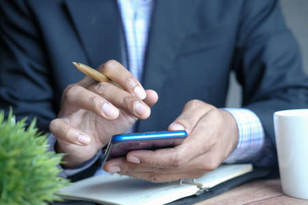 young man hand using smart phone and writing on notepad at deskの写真素材