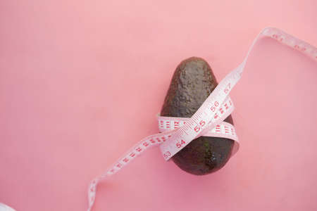 top view of slice of avocado and measurement tape on pinkの写真素材