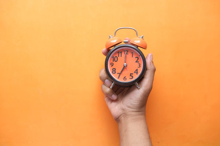 person hand holding alarm clock on orange background ,の写真素材