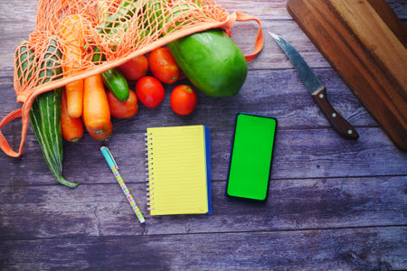 fresh vegetables, cutting board, notepad and smart phone on tableの写真素材