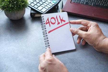 hand hold Notepad with word 401k and laptop on table