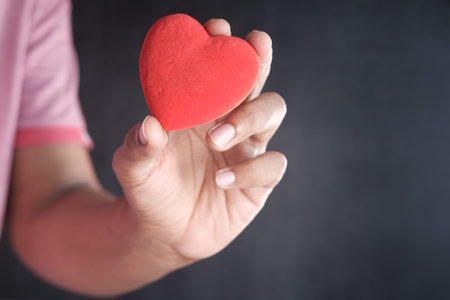 man holding red heart against black background