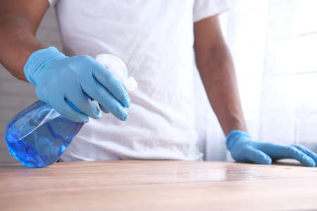 hand in blue rubber gloves holding spray bottle cleaning tableの写真素材