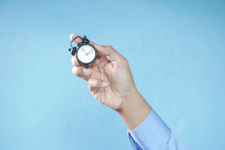 person hand holding alarm clock against blue background ,の写真素材