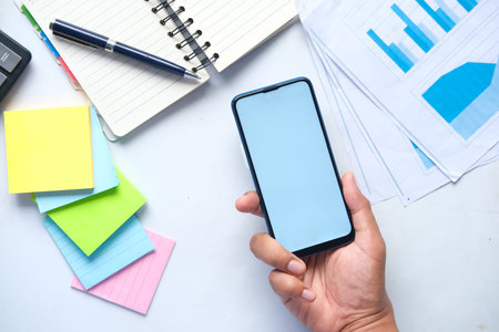 Top view of man hand holding smart phone and office stationary on white
