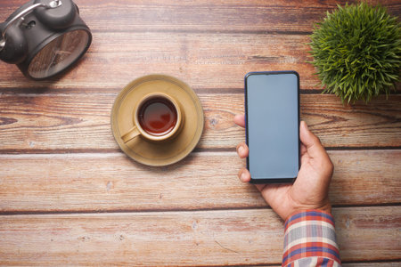 young man hand using smart phone with tea and cookies on table
