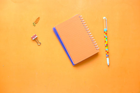 high angle view of orange color notepad with pencil on table