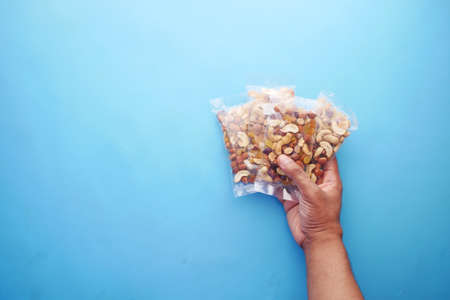 hand hold a packet of mixed nuts on blue backgroundの写真素材