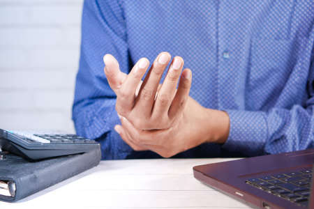 man suffering pain in hand while working on deskの写真素材