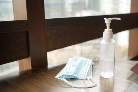 Surgical masks, and hand sanitizer on table against a window