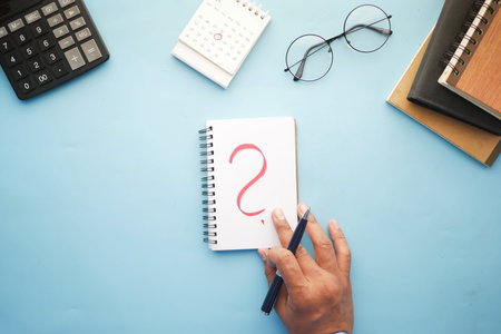 high angle view of hand drawing question mark on paper on office desk