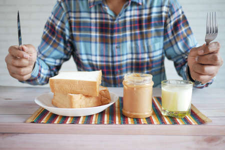 hungry man eating peanut butter, bread and milk on tableの写真素材