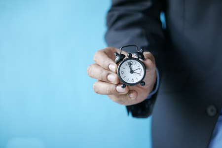 hand holding alarm clock against blue backgroundの写真素材