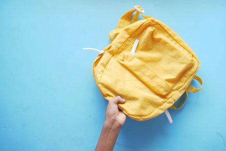 child boy hand holding a yellow backpack on blueの写真素材