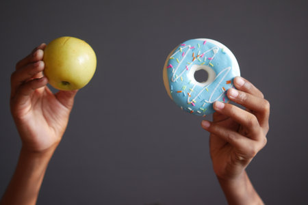 hand holding donuts and apple against gray backgroundの写真素材