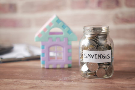 house finance concept with house model and saving coin jar on table