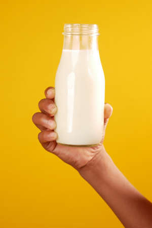 hand hold a milk bottle against yellow backgroundの写真素材