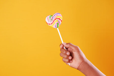 child hand hold a lollipop against yellow background