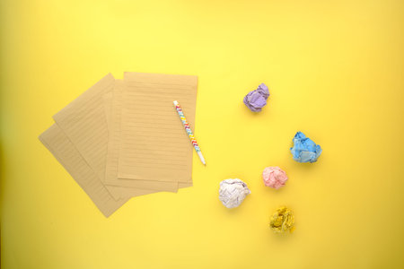 crumpled paper ball and notepad on yellow background