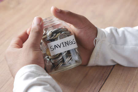 young man hand hold saving coins jarの写真素材