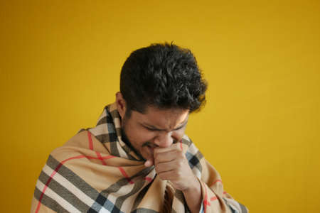 young sick man coughing and sneezes against yellow backgorundの写真素材